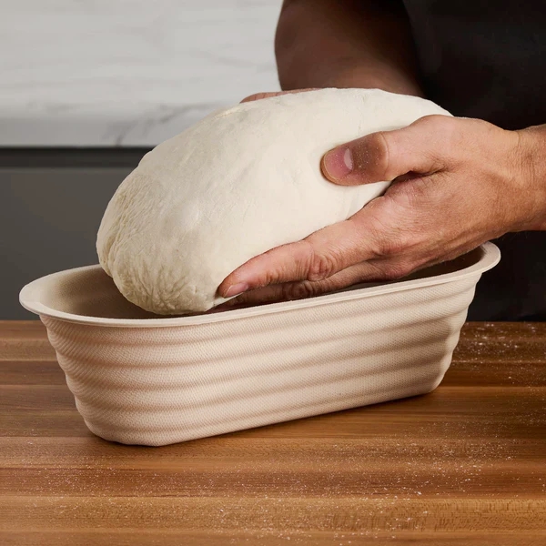 hands putting dough in a batard banneton bowl