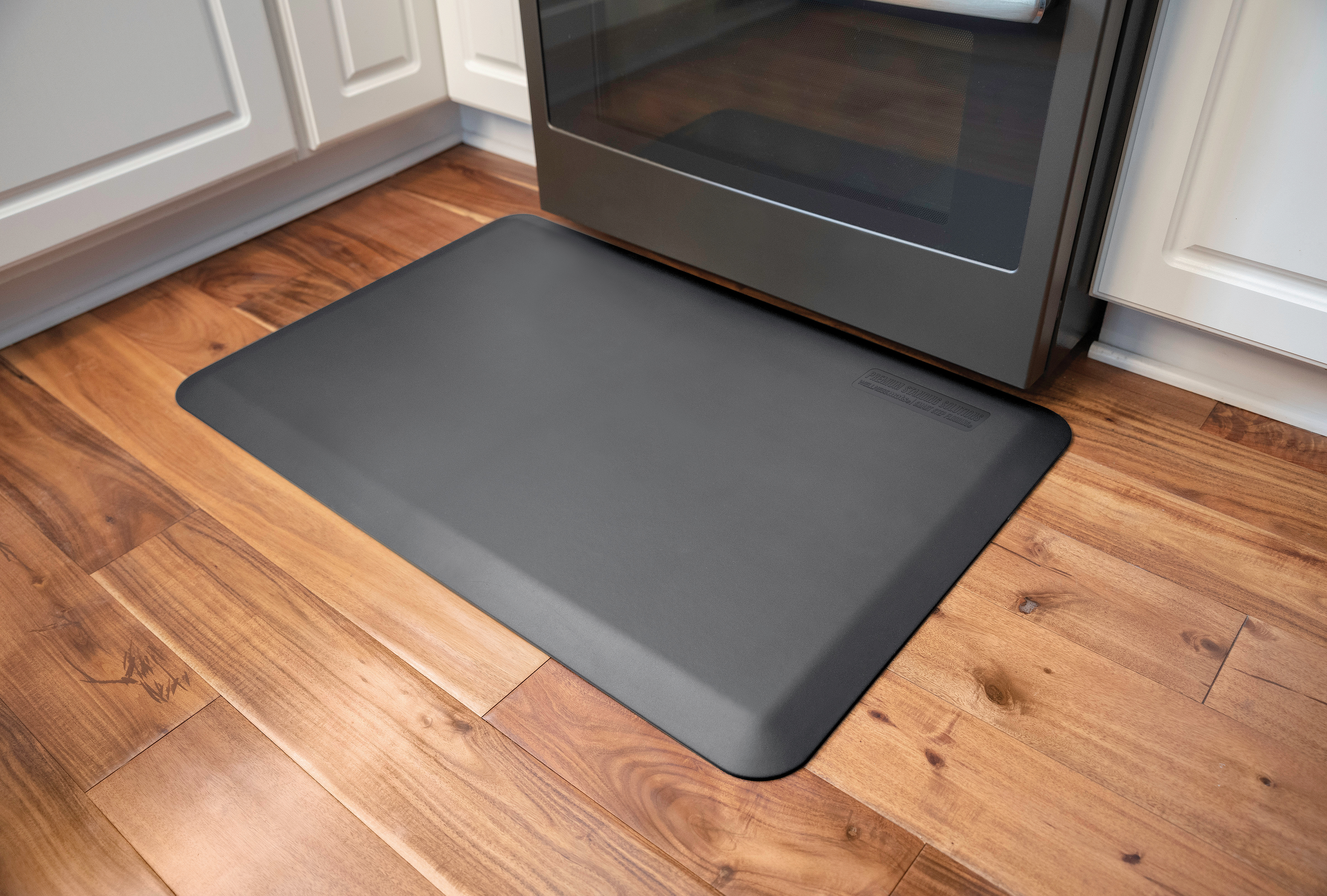 gray wellness mat shown in front of stove in kitchen with wood flooring