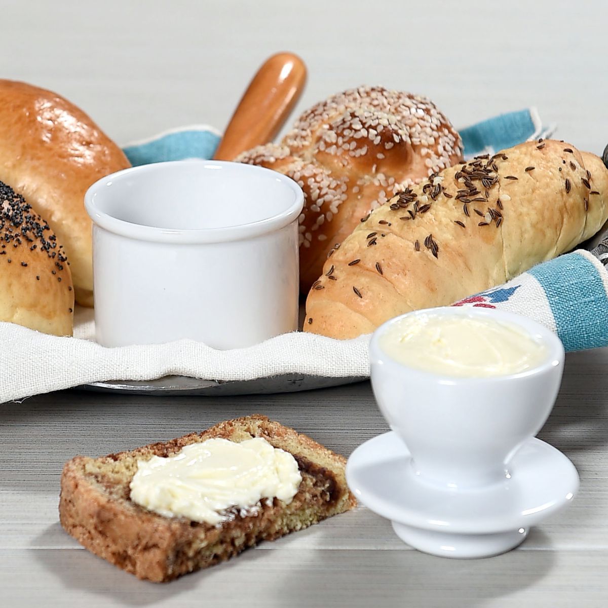 White butter bell junior crock with bell pulled out of crock with basket of bread and a buttered slice.