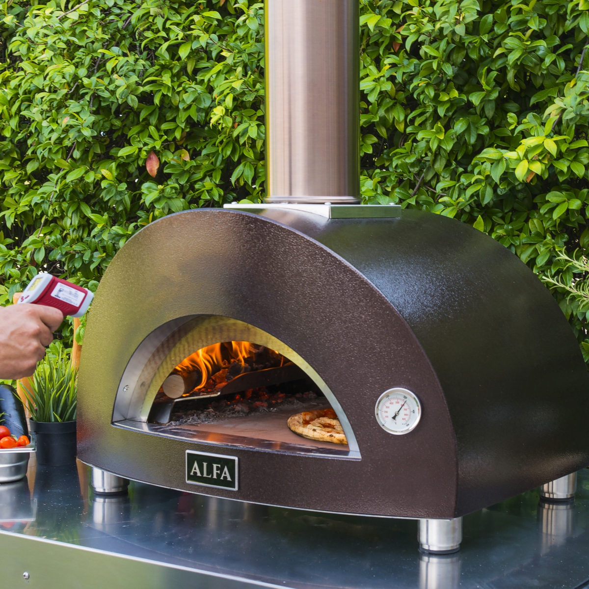 person checking temperature of alfa pizza oven with handheld thermometer in outdoor kitchen
