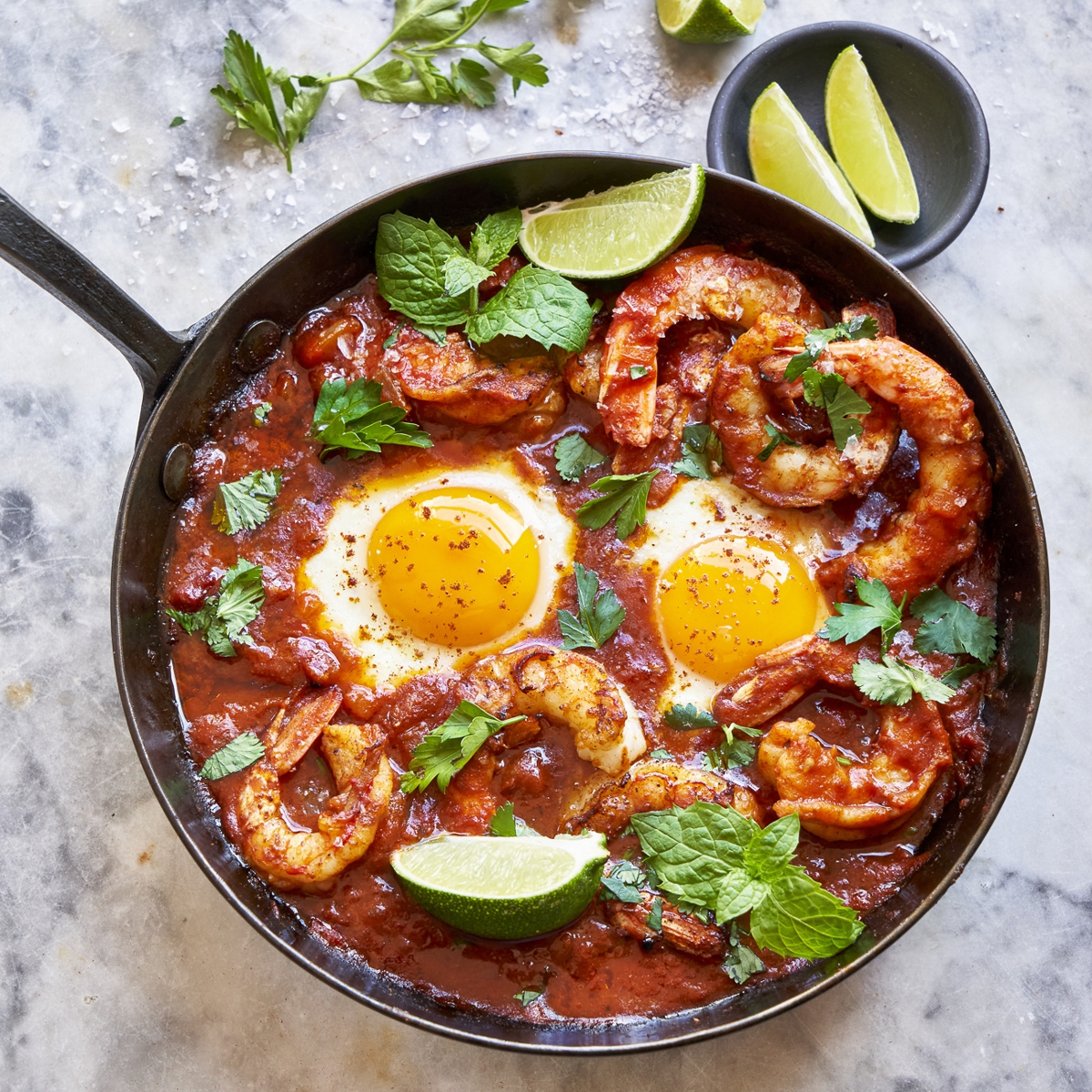 Skillet with seasoned shrimp and eggs garnished with limes