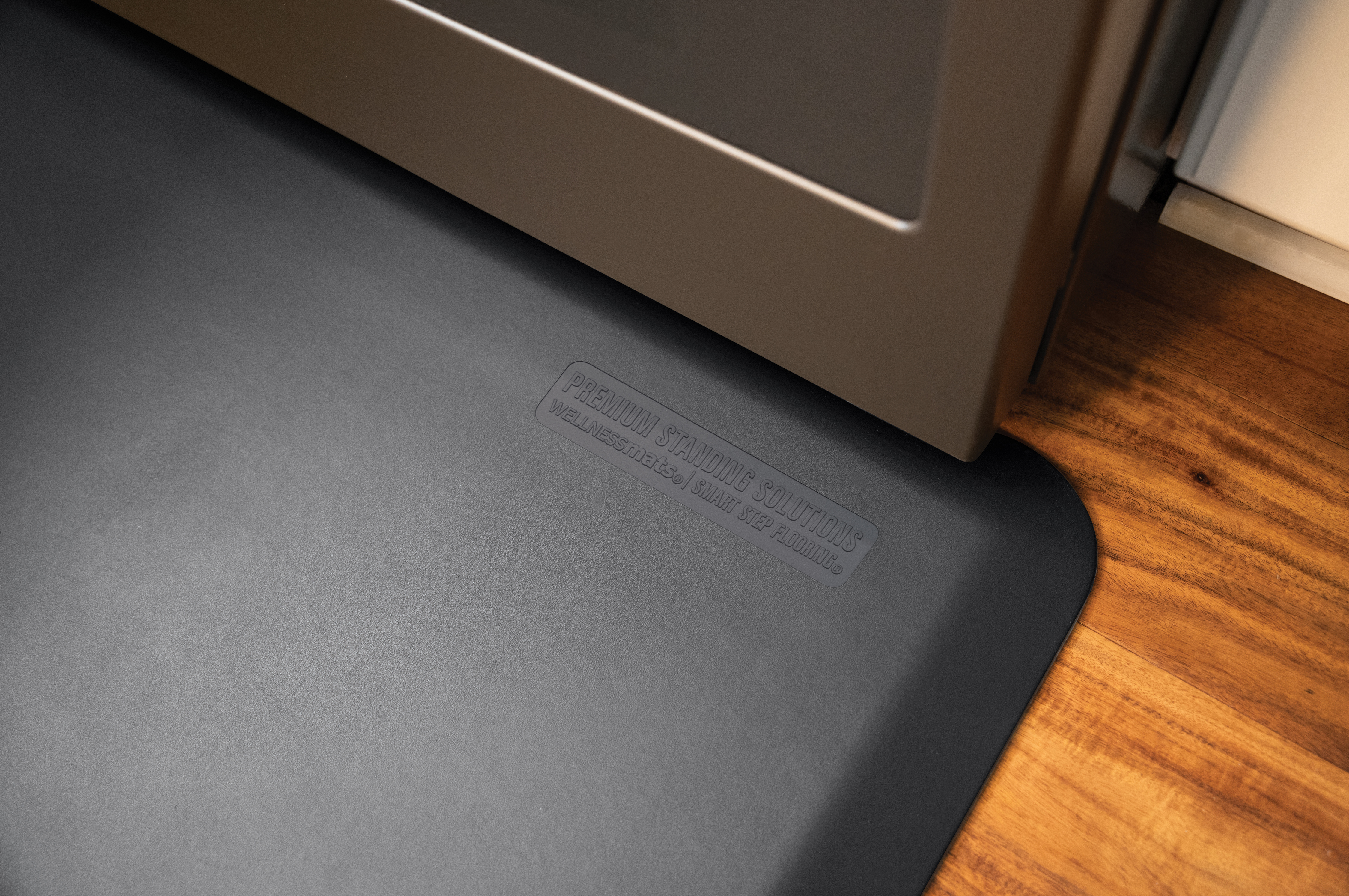 gray wellness mat shown in front of dark cabinets and wood flooring