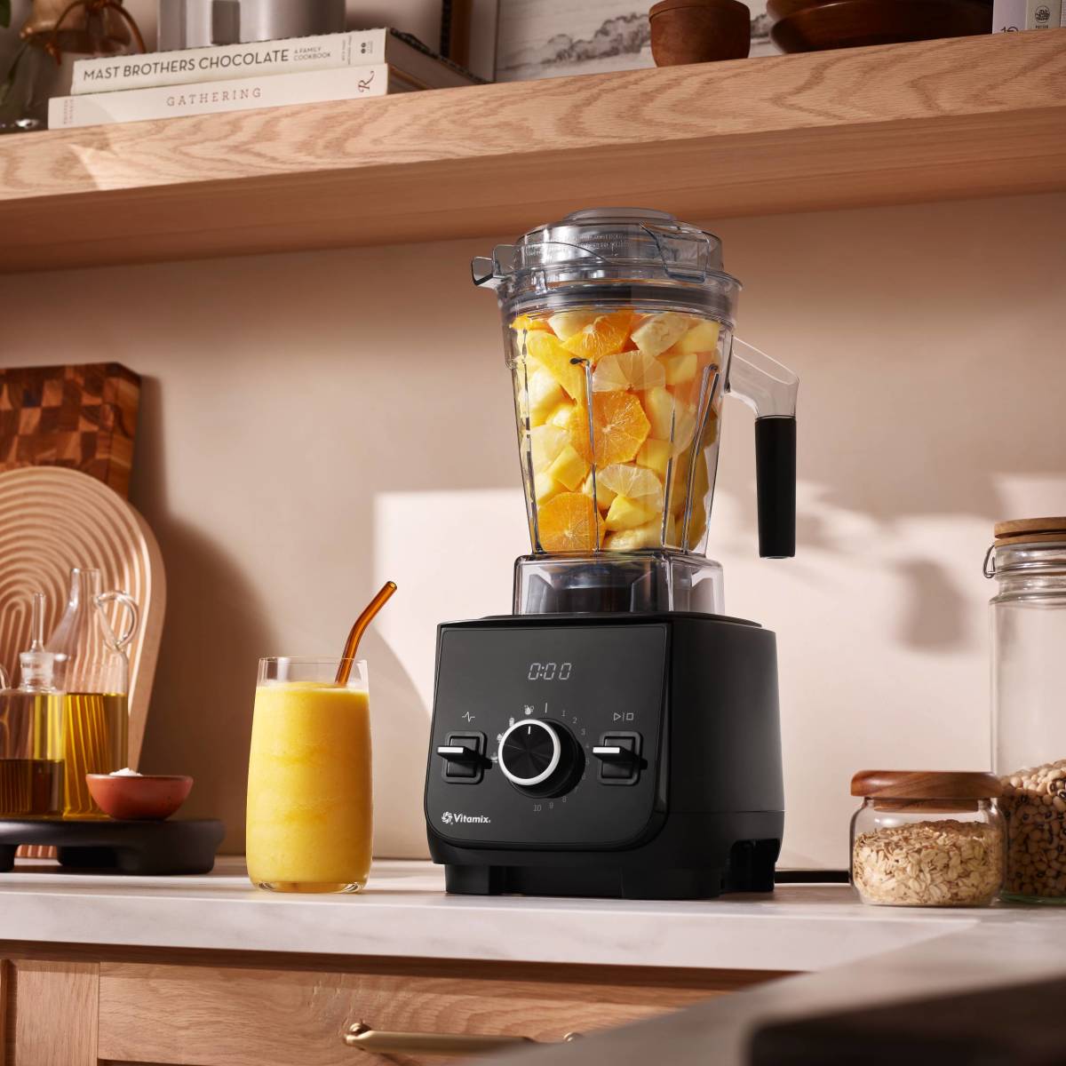 vitamix ascent x2 staged on countertop filled with fruit with glass filled with smoothie next to it